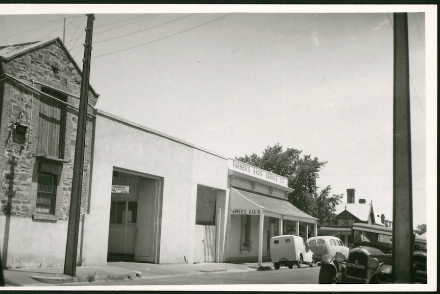 A black and white historical photograph of a building with a couple of cars in front of it