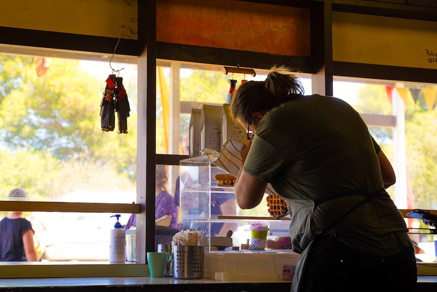 A woman wearing glasses and an apron holding tongs puts a waffle in a glass display cabinet behind large glass windows.