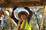 A boy in high-visibility workwear holds up a roof during construction.