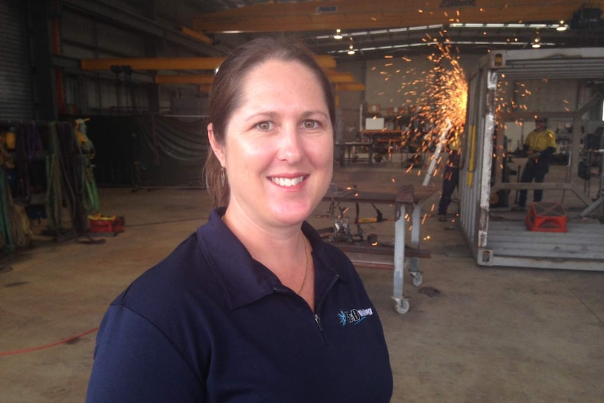 Tracy Ryan stands in a workshop as sparks fly from welding behind her