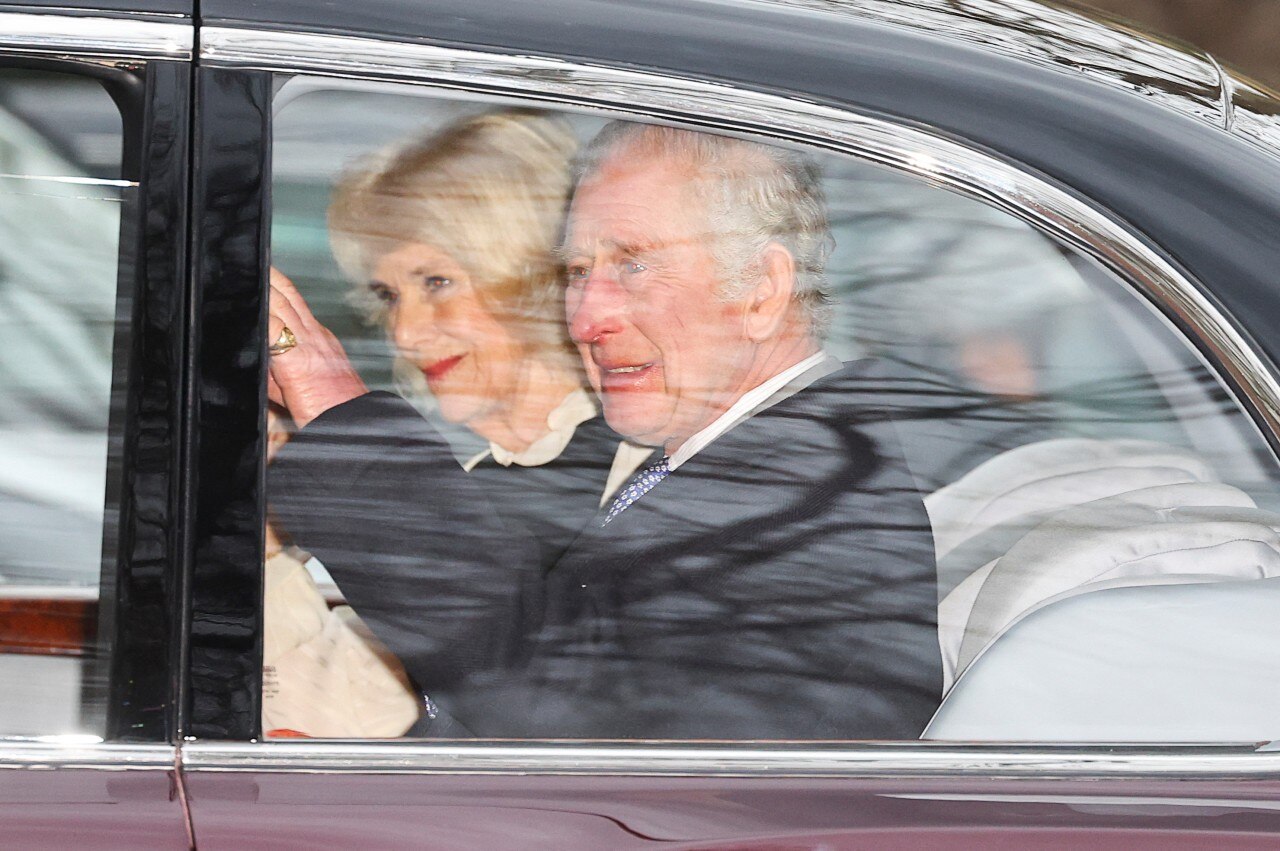 A man and a woman sitting in a car smiling and waving