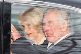 A man and a woman sitting in a car smiling and waving