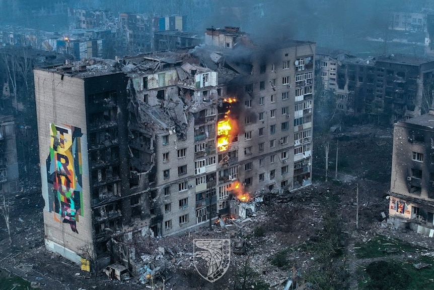 Aerial view shows destroyed multi-storey building with fire and smoke seen on some floors.