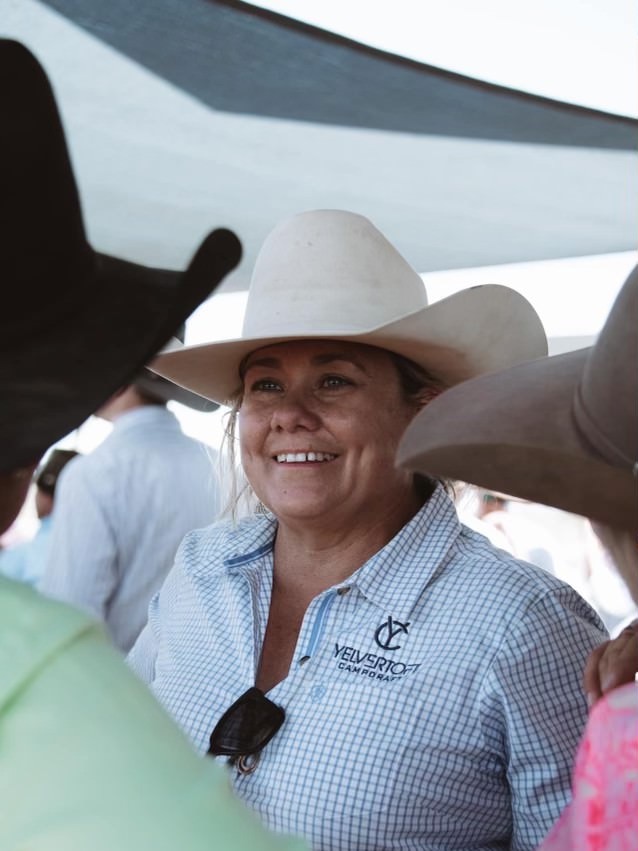 A woman stands smiling looking off into the distance in a cowboy hate 