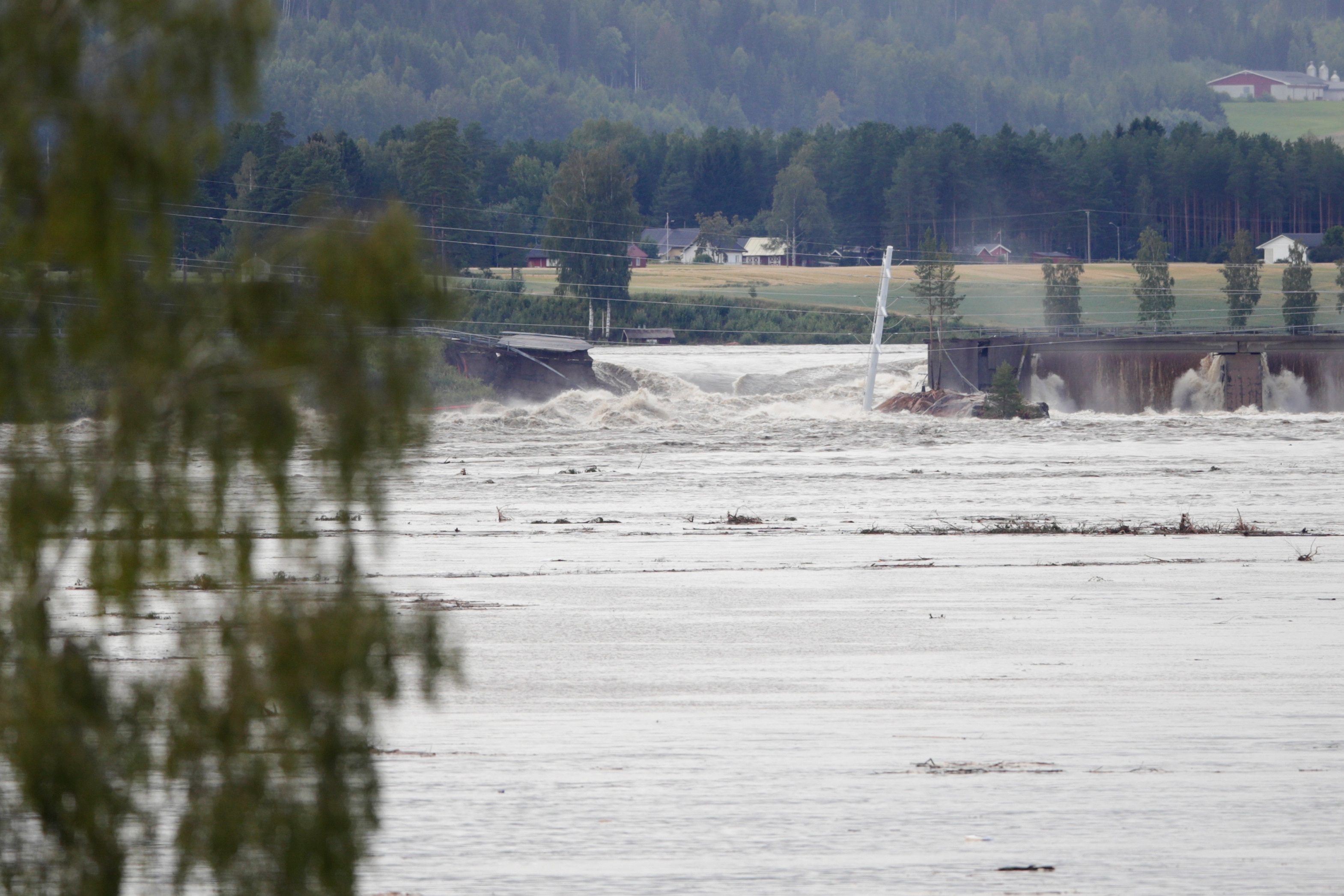 A large area of land coverd with water gushing through a hole in a a dam's wall with mountains in the distance