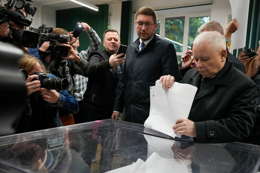 Jaroslaw Kaczynski placing a voting slip in a ballot box surrounded by cameras. 