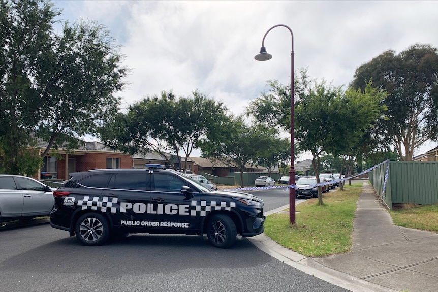 Police car parked over a street with police tape