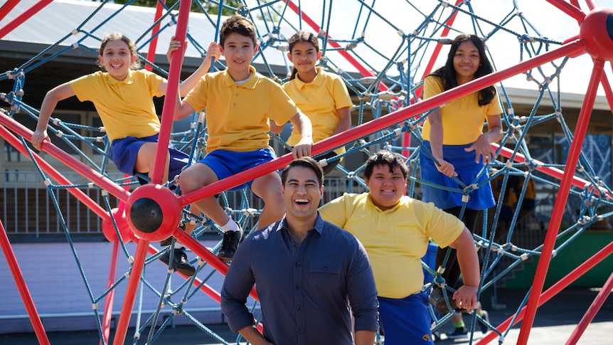 A man at a school with students climbing in the playground.