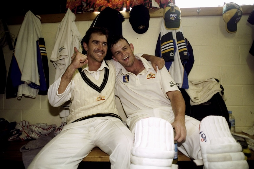 Justin Langer and Adam Gilchrist sit in the change room smiling with an arm around each other