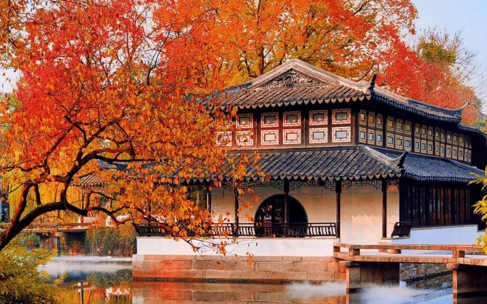 A traditional Chinese building beside a lake and trees in red autumn colours.