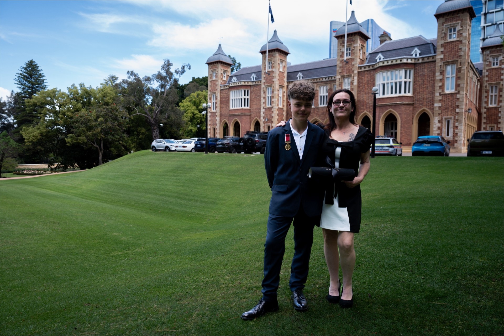 Austin Appelbee with a medal on his chest and his mother Joanne holding a certificate stand outside WA Government House.