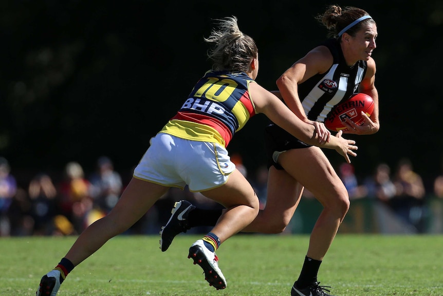 An AFLW player runs with the ball, putting her hand on the arm of a defender to break a tackle.
