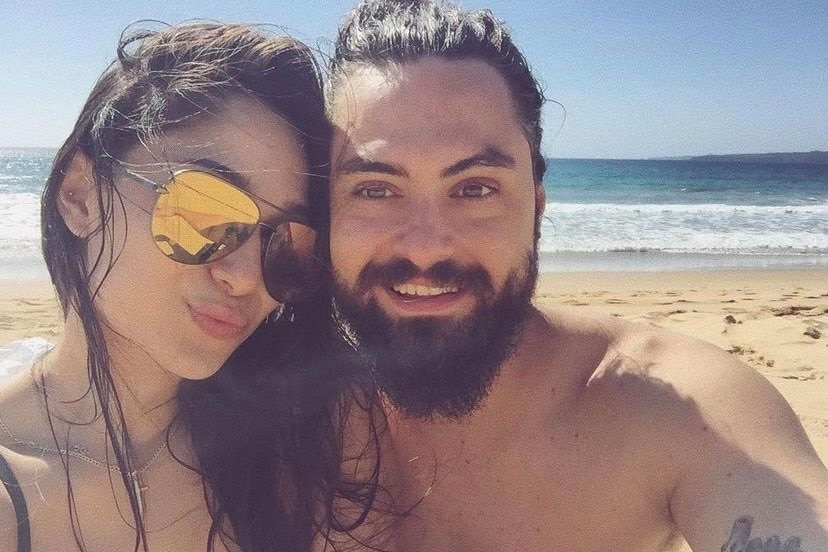 A man and a woman take a selfie on the beach.