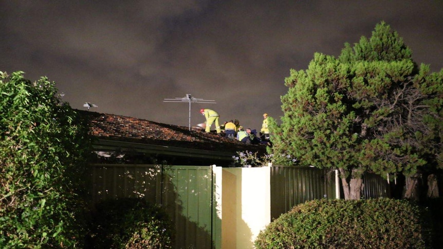 Emergency services workers in fluoro jackets on the tiled roof of a Yokine house at night.
