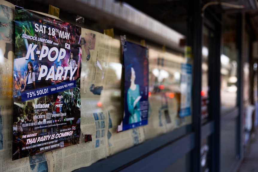 A poster advertising a K-Pop party is plastered on a window which is covered in old newspapers, concealing the insides.