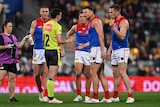 An AFL umpire holds his hand out towards a Melbourne player who is arguing with him, as other Demons players surround him.