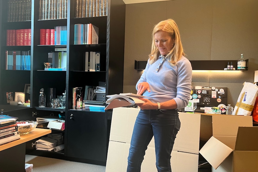Fiona Patten holding a book in an office, with boxes behind her.