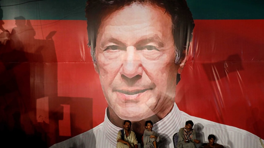 Workers sit in front of a huge Imran Khan billboard.