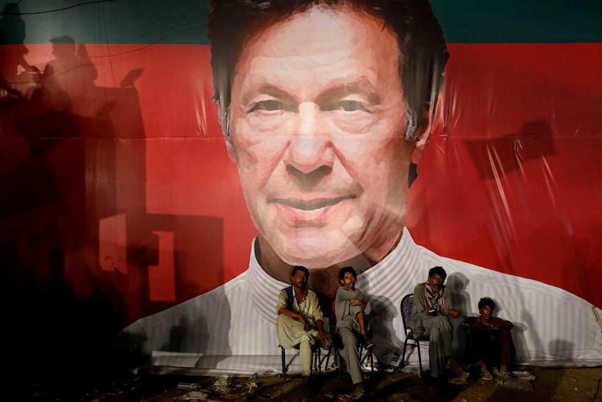 Workers sit in front of a huge Imran Khan billboard.