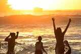 Silhouetted revellers frolic in the water as the sun rises over Bondi Beach.