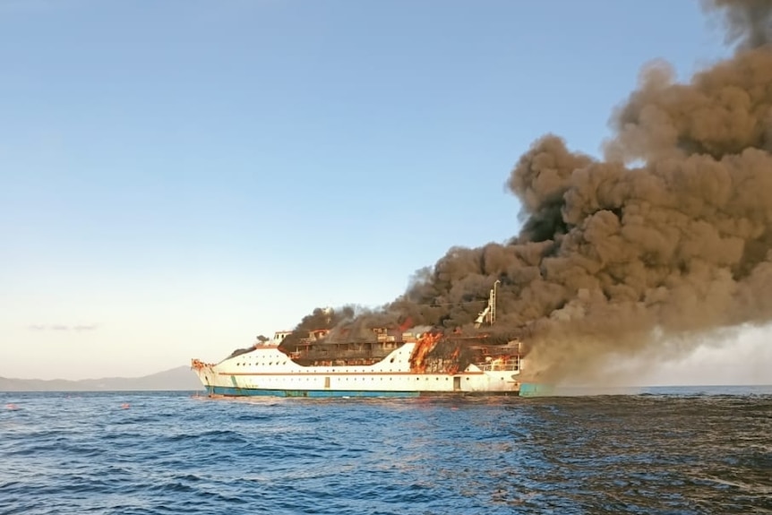 A ferry is in flames on the ocean.