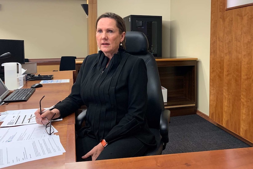 A magistrate sits on the bench of a court room wearing a black top.