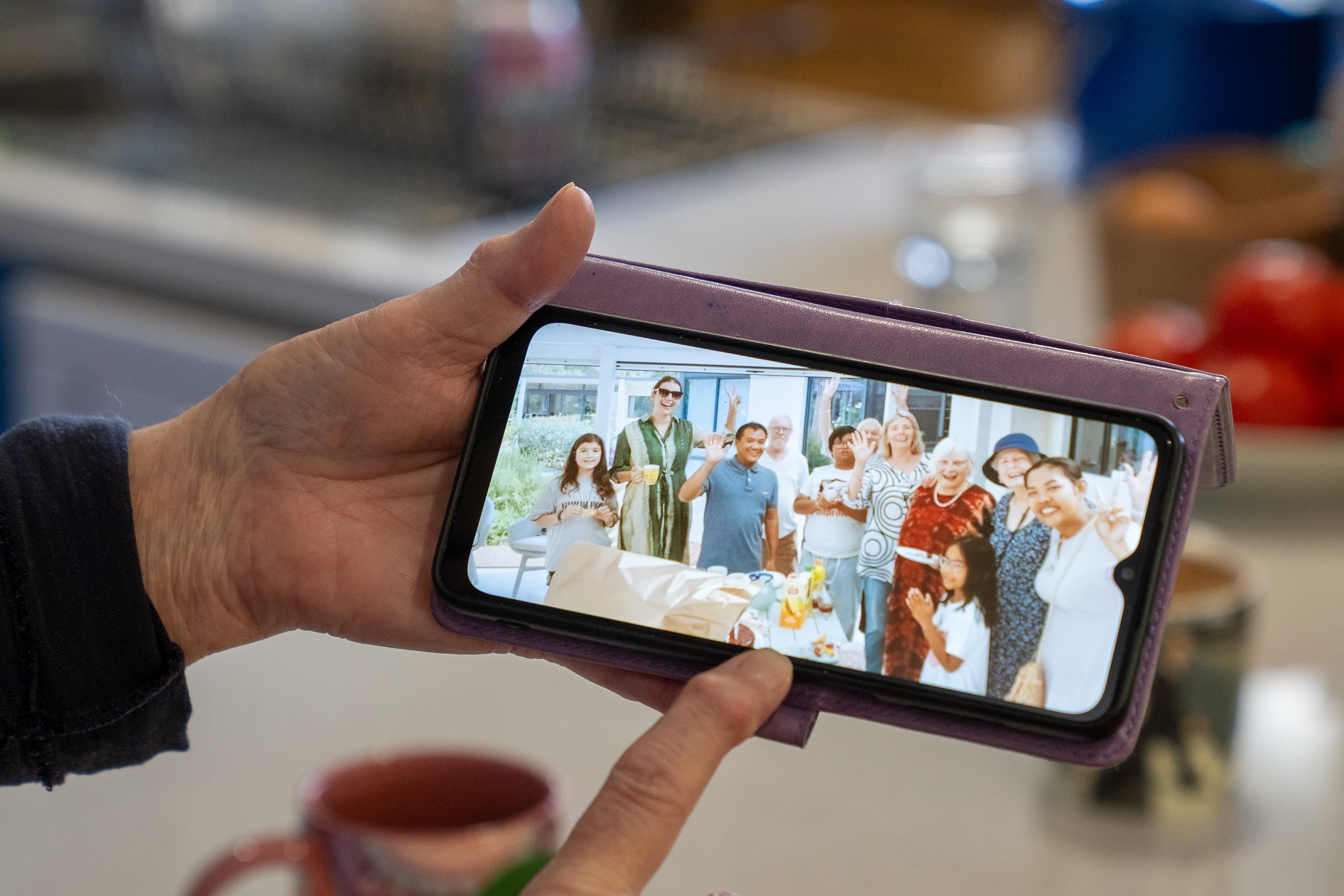 A person's hand holding a phone held in landscape showing a photo of a group of people, smiling