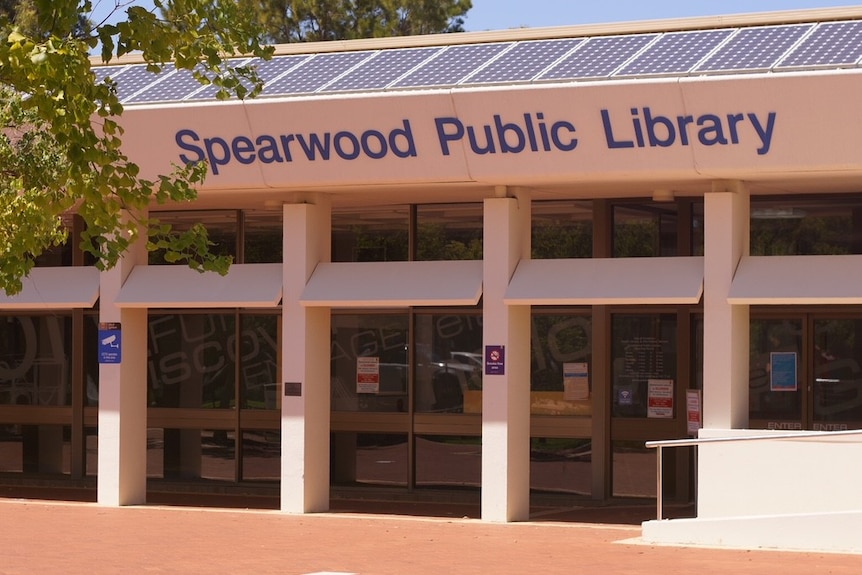 The front exterior of Spearwood Public Library, which features large glass windows and pavement and trees on approach.