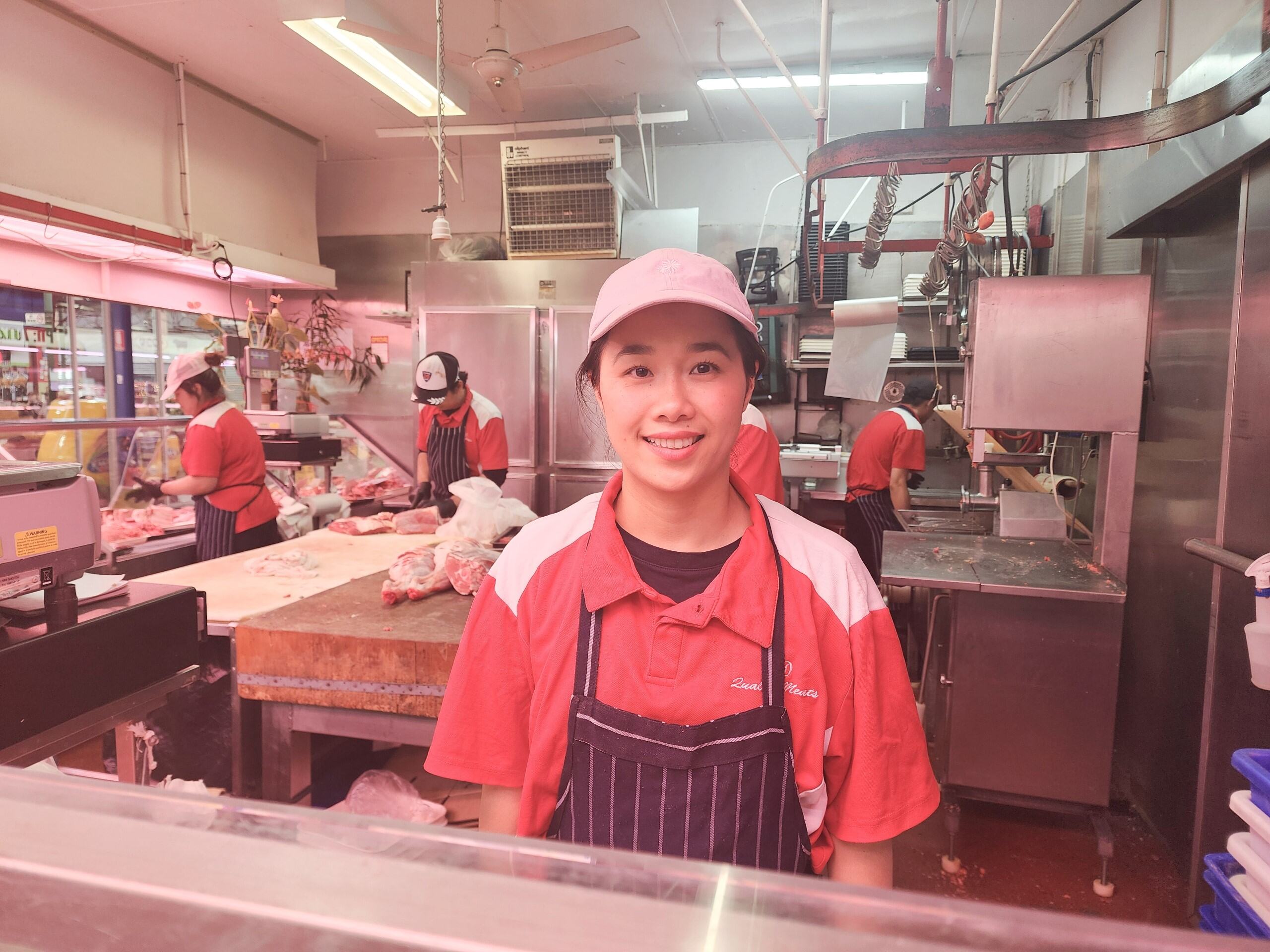 A young lady at a butcher with staff working behind her