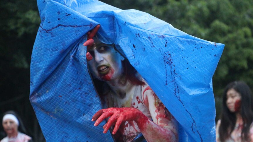 A female zombie emerges from a makeshift body bag