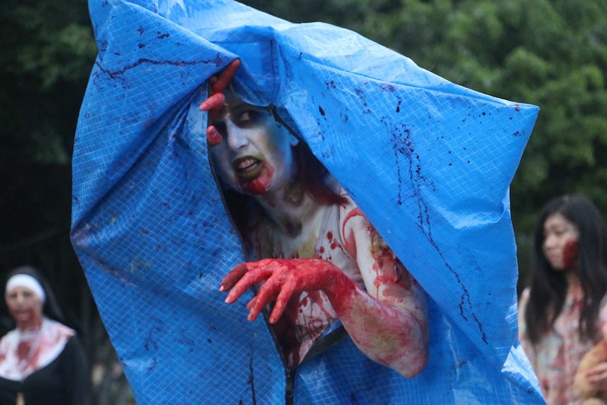 A female zombie emerges from a makeshift body bag