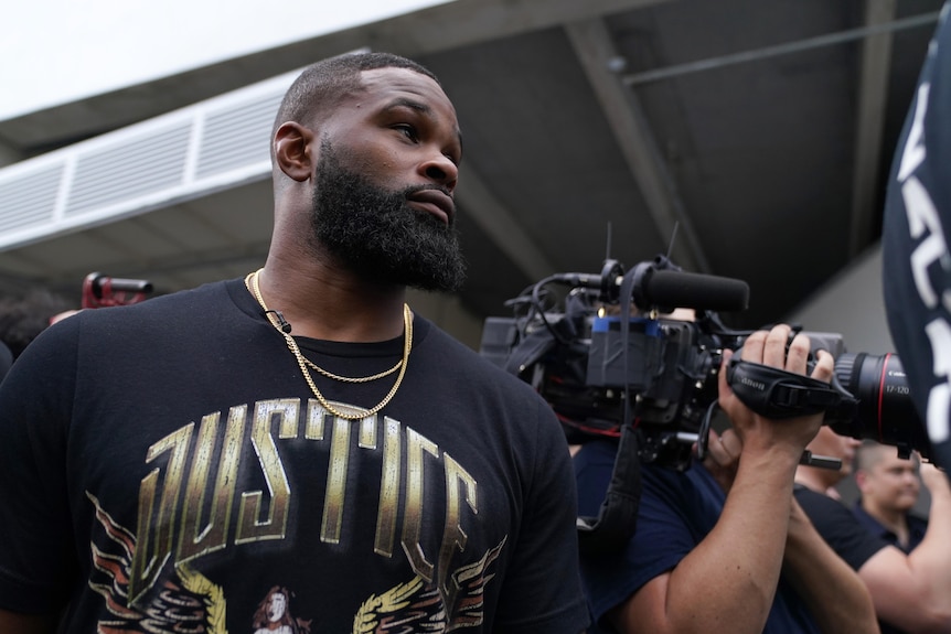 A man in a black shirt in front of cameras.