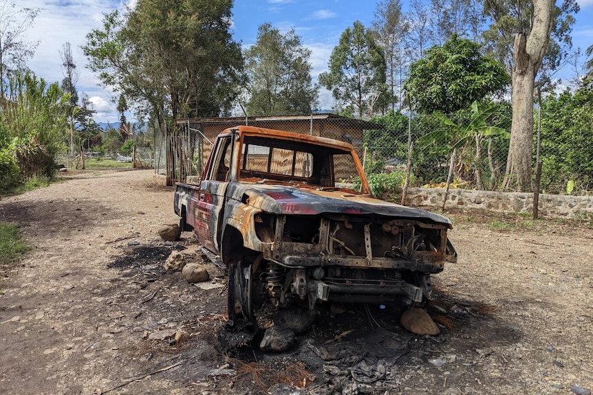 The burnt out shell of a utility vehicle on a dirt road. 