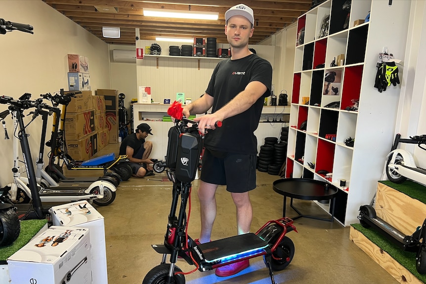 A young man stands in a scooter shop holding a scooter.