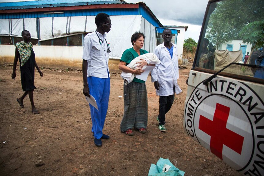 A nurse carries the body of baby Nyanene to a Red Cross vehicle. The baby's mother follows behind.