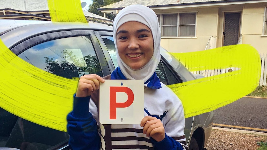Woman stands next to her car holding her P-plates for a story about helping refugees get their drivers licence in regional Aus.