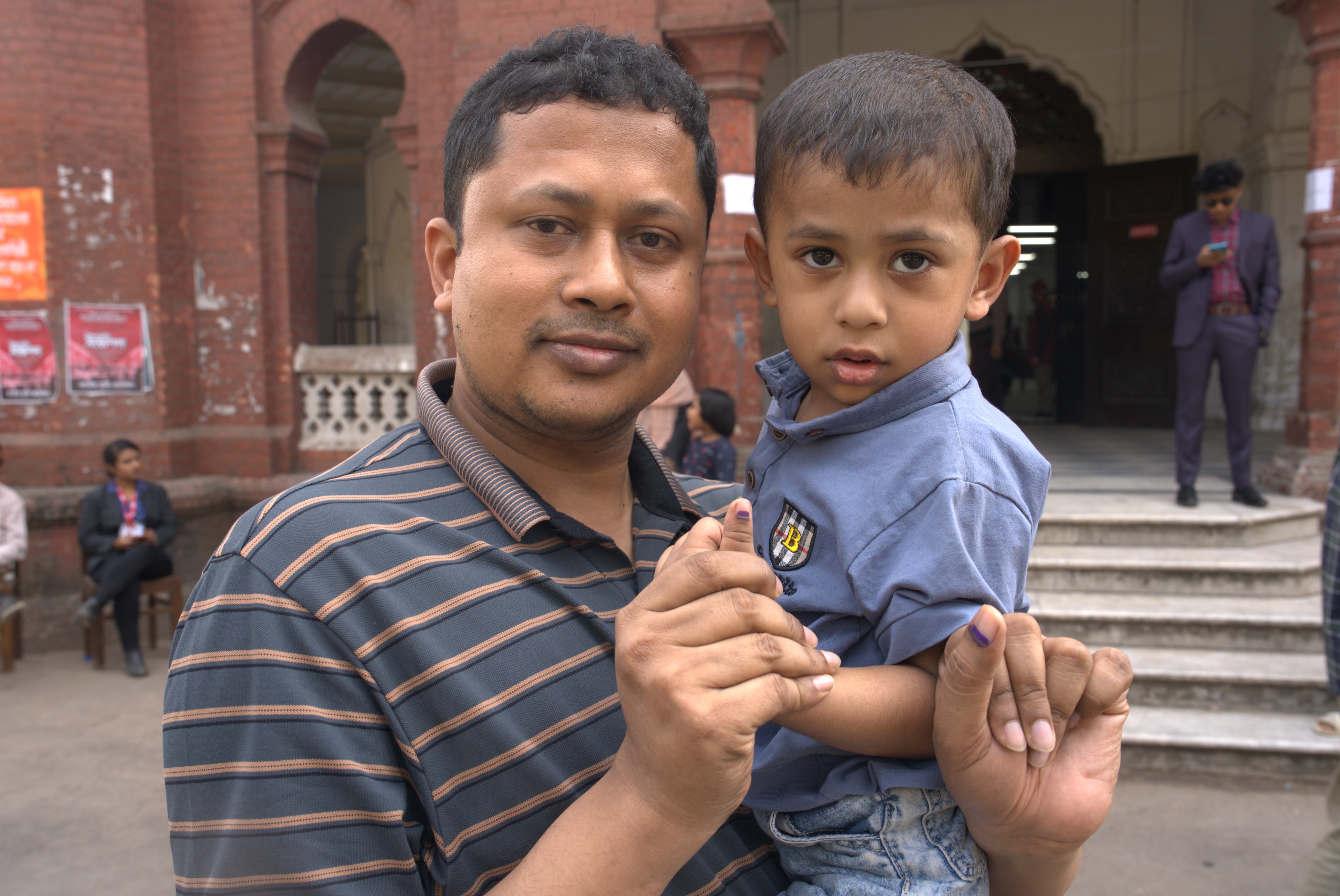 Un hombre sostiene a su hijo y muestra su dedo vendado a la cámara.