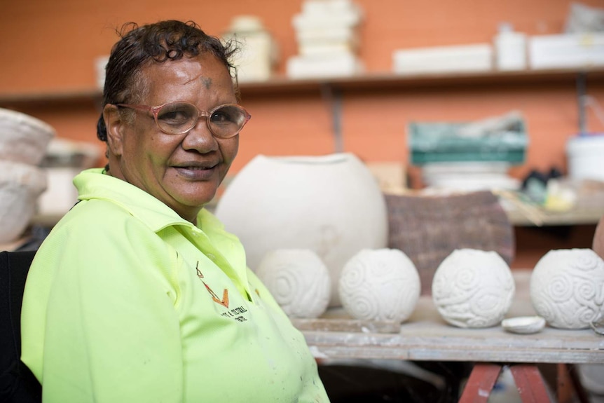 Aboriginal artist Michelle Yeatman smiles for a photograph in front of her pottery.