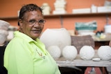 Aboriginal artist Michelle Yeatman smiles for a photograph in front of her pottery.