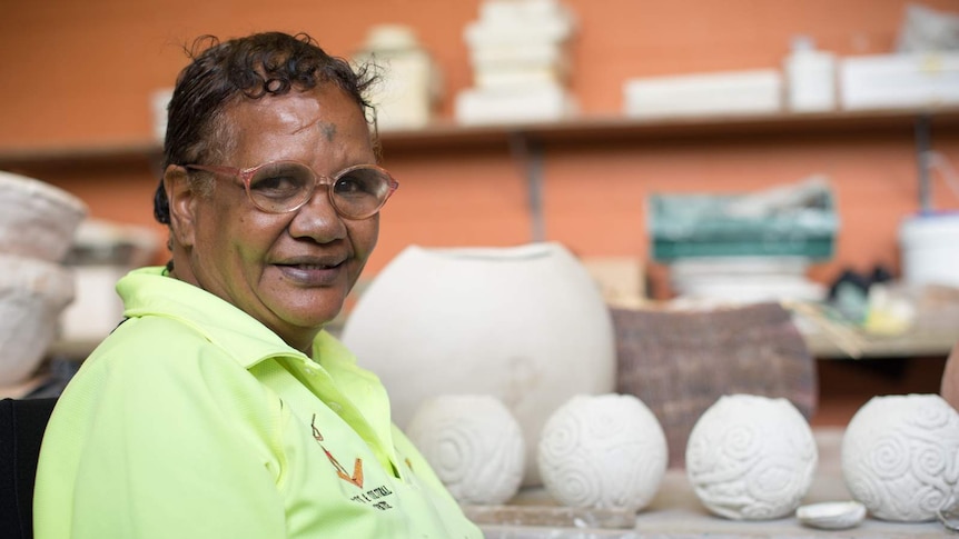 Aboriginal artist Michelle Yeatman smiles for a photograph in front of her pottery.