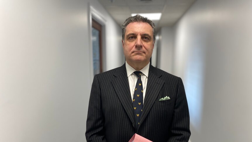 A man wearing a suit holding a folder standing in a hallway