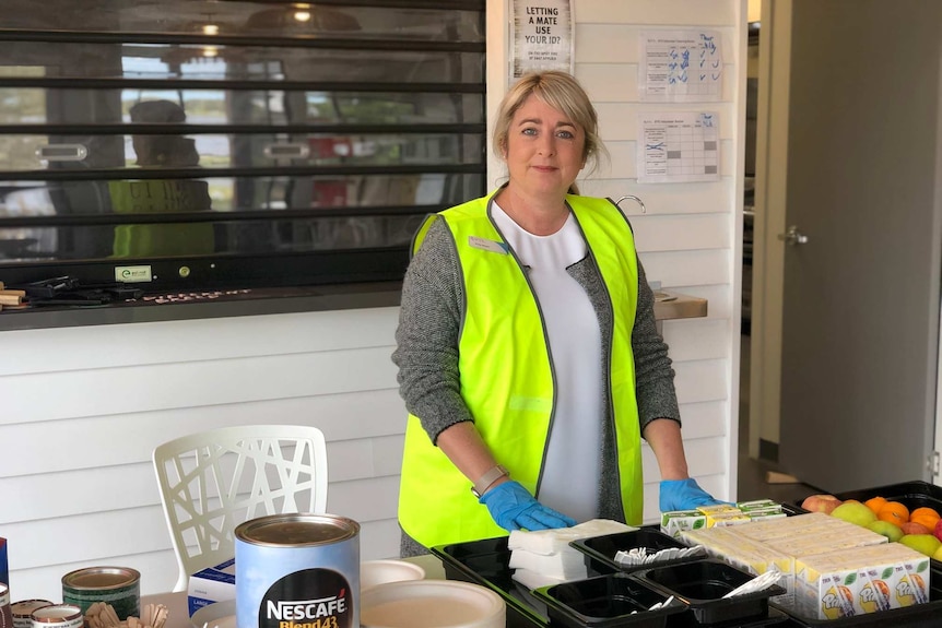 A woman in a high-vis vest smiling, standing over a table with food on it.