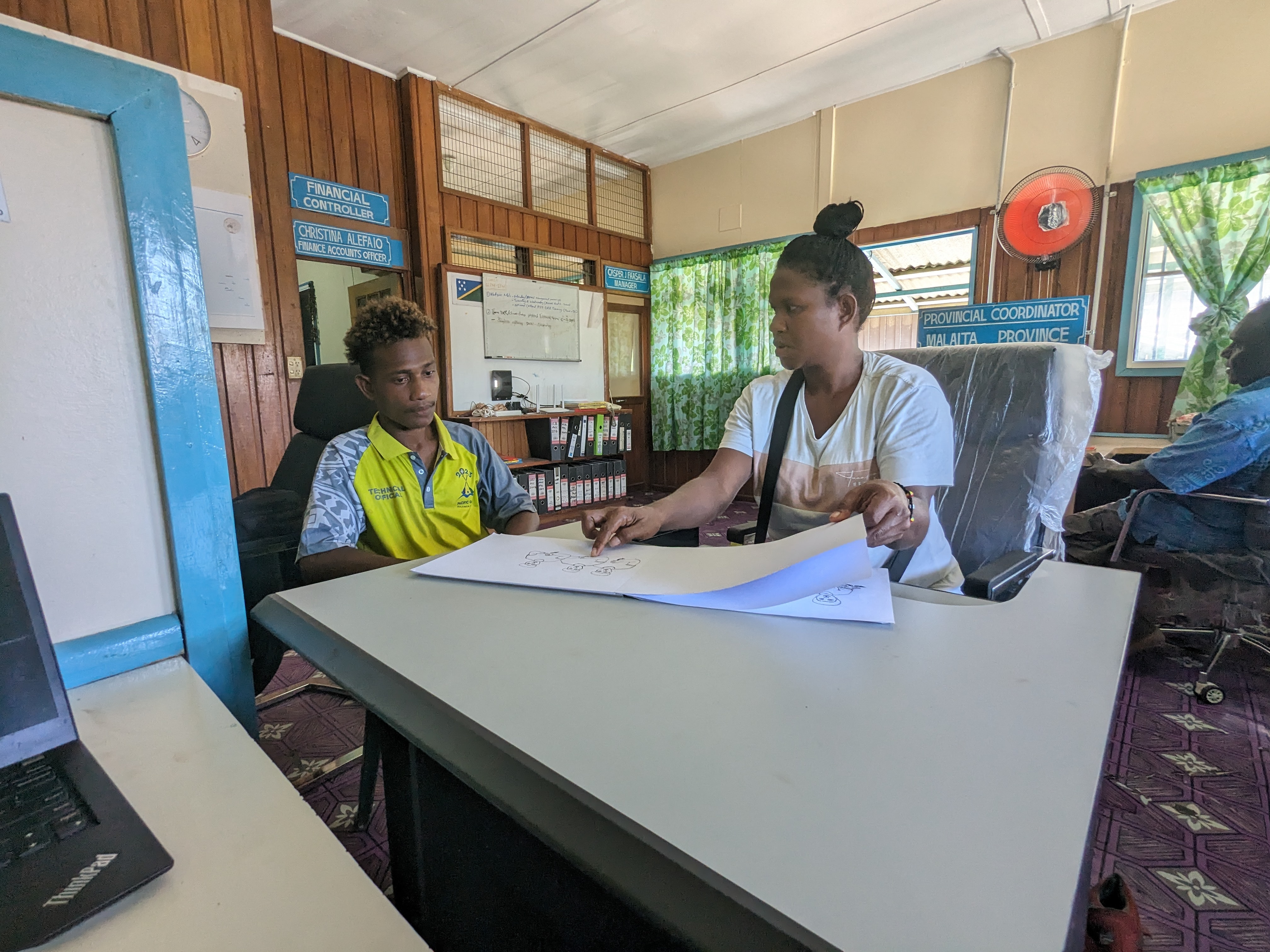 Woman sits at table holding pages next to man inside a room. 