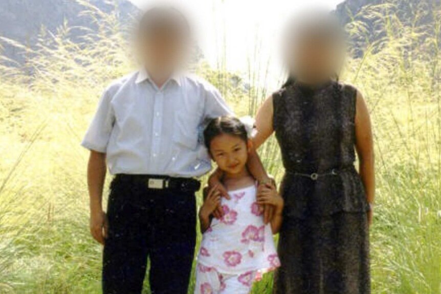 A little girl stands with her parents. Their faces are blurred