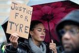 A black woman with eyes closed holds an umbrella and a sign saying "Justice for Tyre"