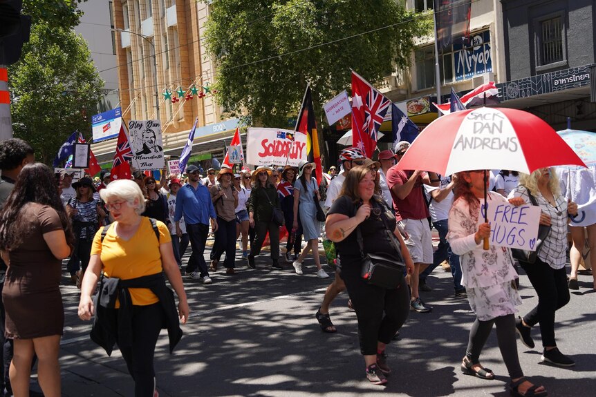 People hold placards and flags as they march through Melbourne streets.