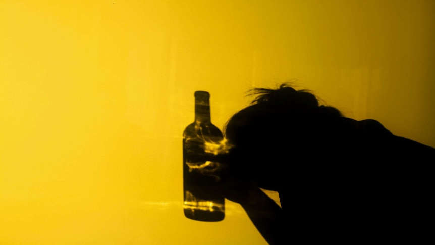 The silhouette of a woman holding a bottle of spirits with her head in her hands