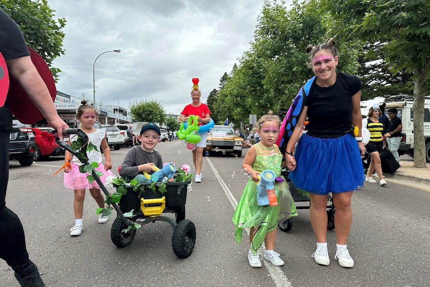 three kids and adults dressed colourfully parading on the road.
