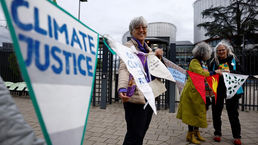 Supporters of the Senior Women for Climate Protection smile and hold banners as they arrive at the court