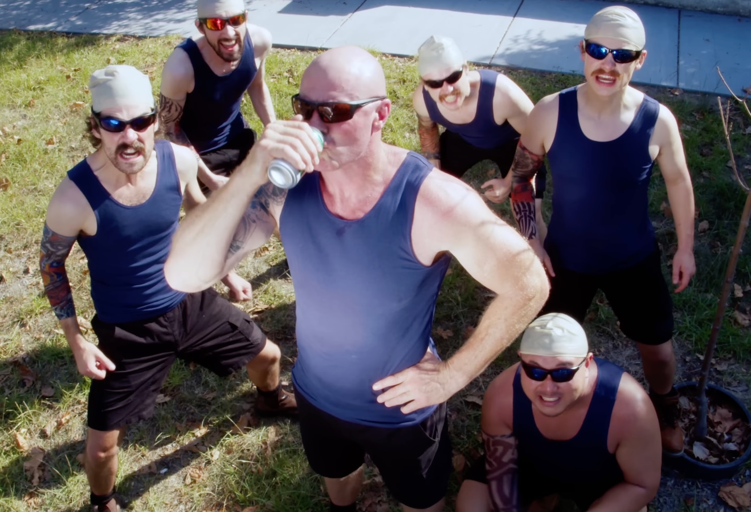 Barry Hall bebe una lata de cerveza con una camiseta azul, rodeado de hombres calvos que llevan la misma camiseta.